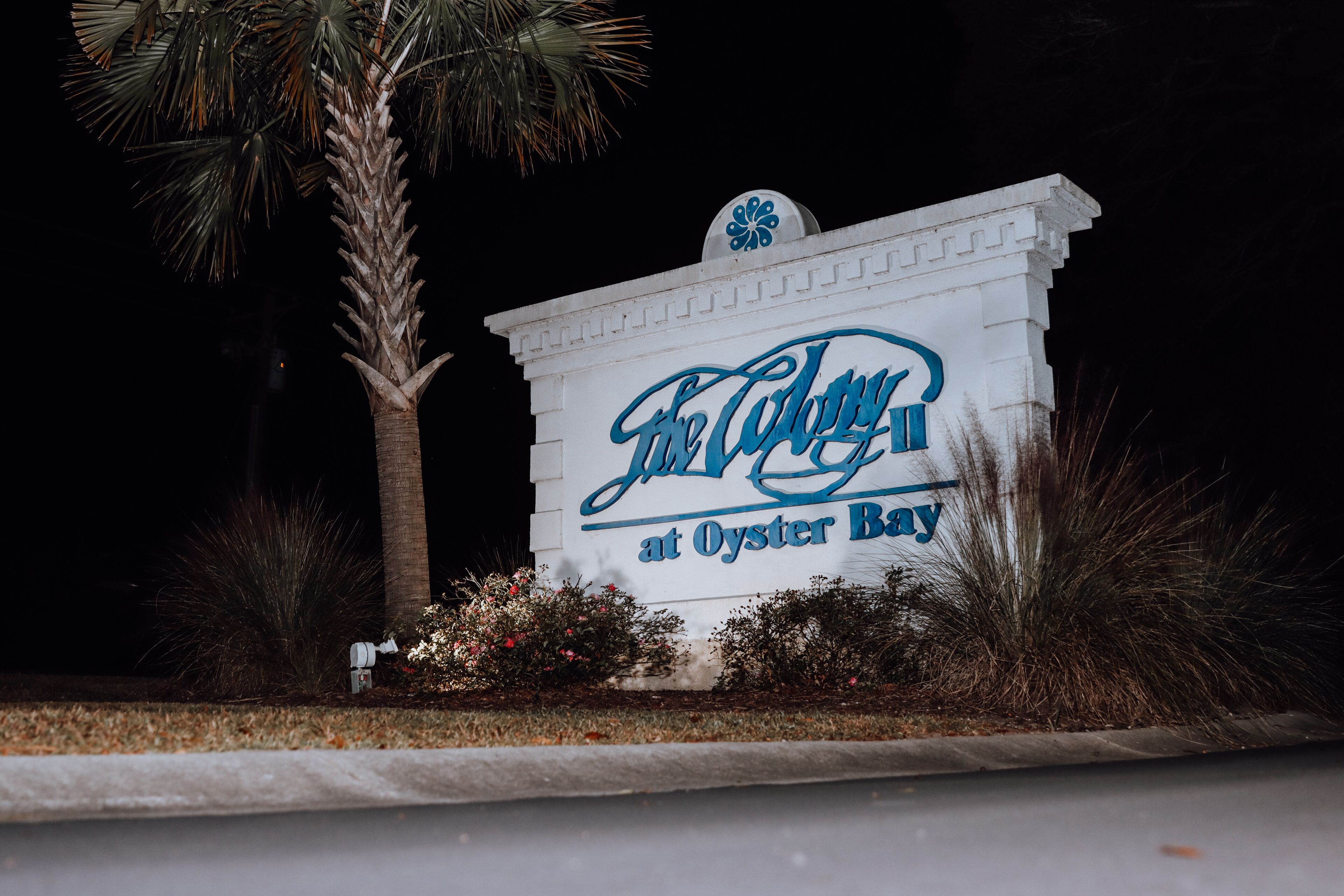 A sign for 'The Culver at Oyster Bay' with a palm tree and some bushes in the foreground.