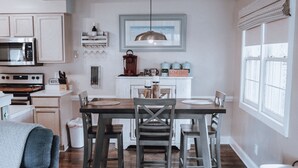 Een keuken met houten kastjes, een roestvrijstalen magnetron, een koffiehoek en een eettafel met stoelen.
