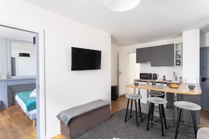 Ein kompakter Wohnbereich mit Küchenzeile, einer Sitzbank und einem an der Wand befestigten Fernseher.