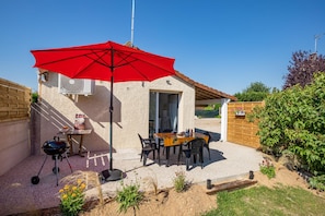Un patio con una parrilla, una mesa con sillas y un paraguas rojo.