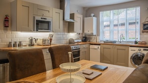 A modern kitchen with a microwave, oven, and dishwasher. There is a dining table with chairs and a coffee maker. - Ironmasters House (Telford)