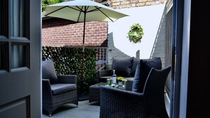 An outdoor patio area with wicker furniture, a table with drinks, and a large umbrella. - Ironmasters House (Telford)