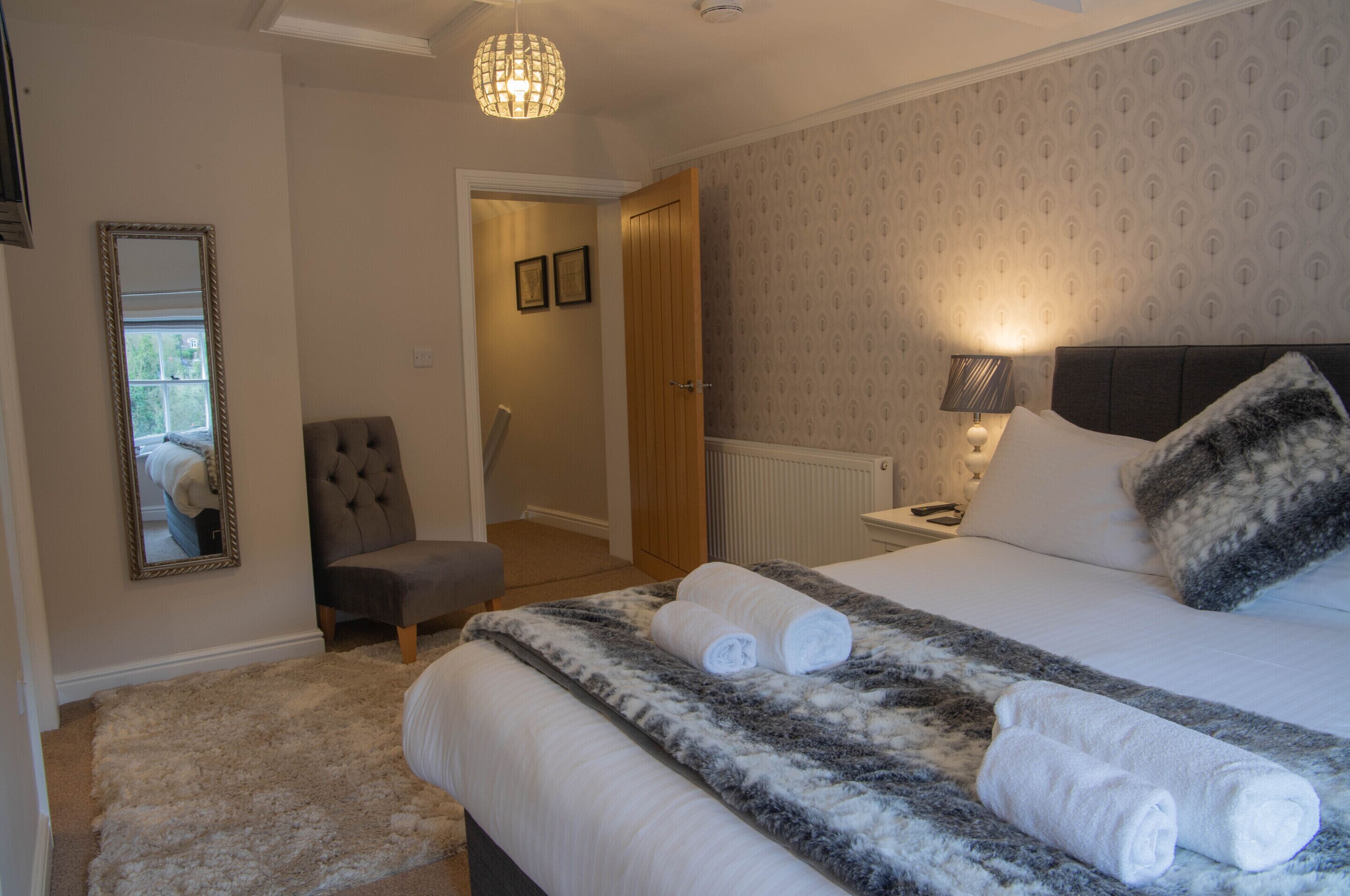 Una habitación de hotel con cama, una silla, un espejo y una puerta que da a otra habitación.