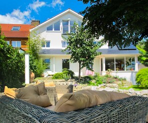 Enjoy the expansive balcony and porch area with a wicker sofa, perfect for relaxing amidst the beautifully maintained garden.