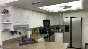 A modern kitchen with white cabinets, a stainless steel refrigerator, a microwave, and a coffee maker. - 2-Bedroom Condo Steps to Beach, Pools, and Golf (Fort Pierce)