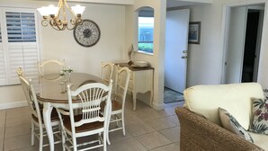 A dining area with a round table, white chairs, a chandelier, and a wall clock. - 2-Bedroom Condo Steps to Beach, Pools, and Golf (Fort Pierce)