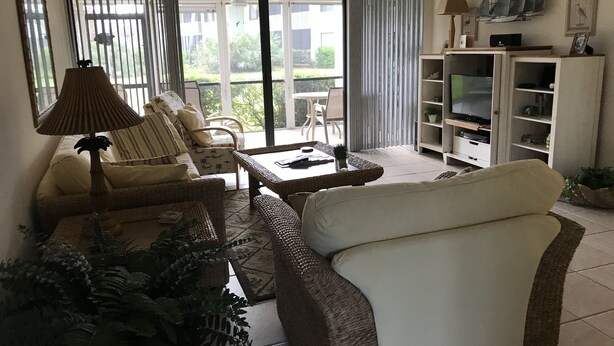A living room with a sofa, armchairs, a coffee table, and a TV stand. - 2-Bedroom Condo Steps to Beach, Pools, and Golf (Fort Pierce)