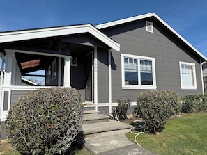 A residential house with a front porch, a garage door, and a well-maintained lawn.