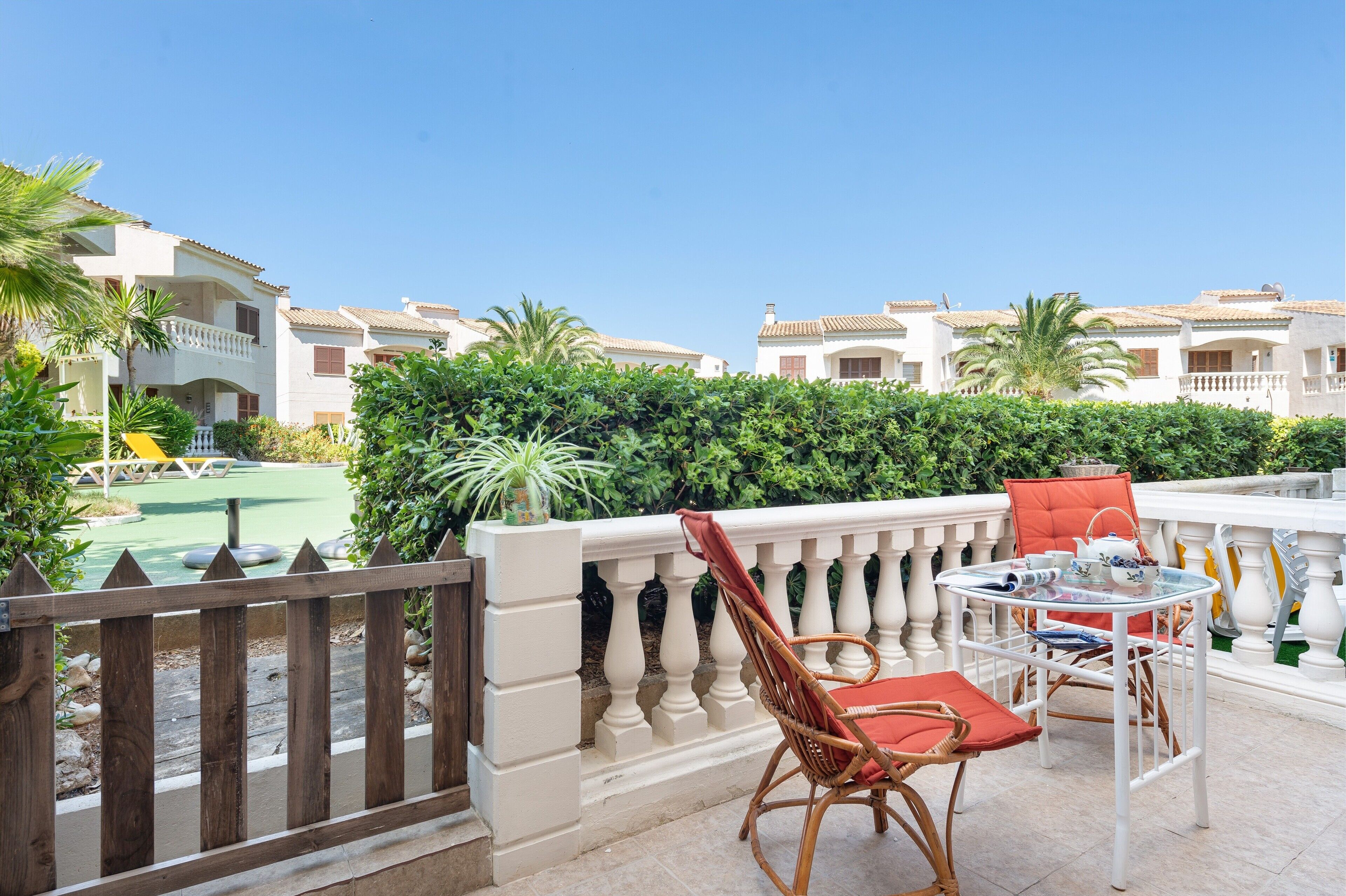 Un balcone con sedie in vimini e un tavolo, con vista su una piscina e un edificio con balconi.