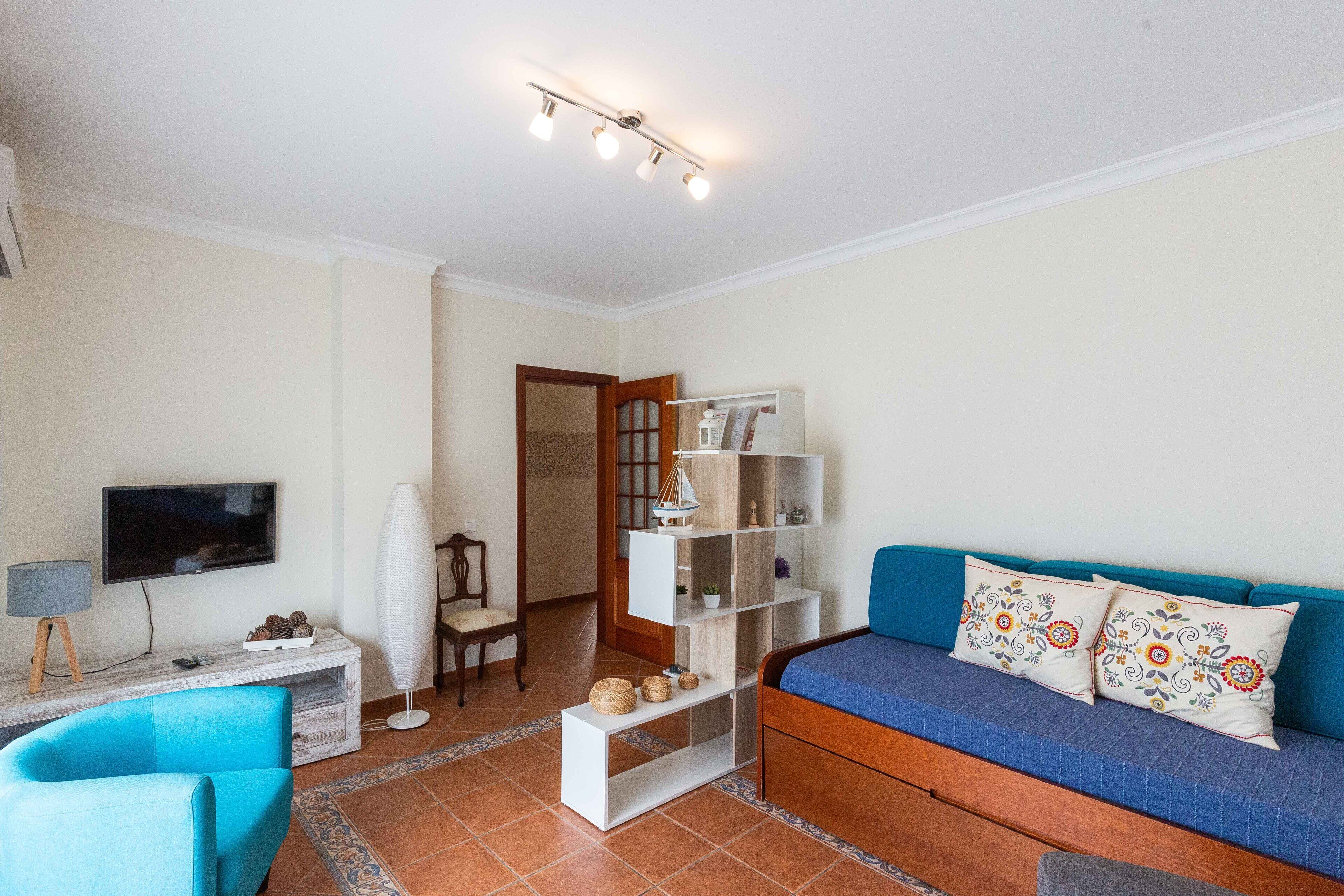 A living room with a TV, a blue sofa, a white shelving unit, and a blue chair.