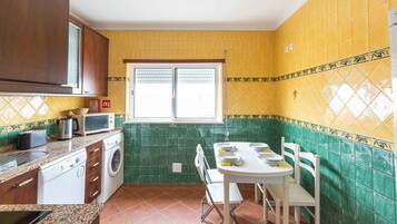 Una cocina funcional con lavadora, microondas y una mesa de comedor con sillas.