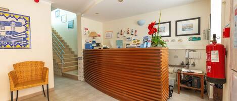 A reception area with a wooden reception desk, a wicker chair, a staircase, and various wall decorations including framed pictures and a welcome sign.