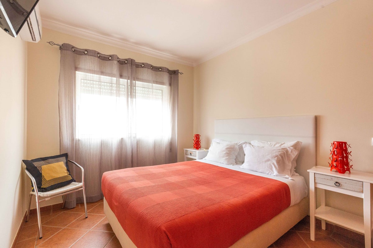 A neatly arranged hotel room with a large bed, a chair, a nightstand, and a television mounted on the wall.