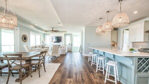 Une cuisine spacieuse dotée d’un grand îlot central, de planchers en bois et de luminaires suspendus.