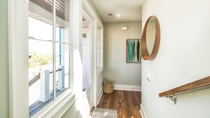 Un couloir avec un plancher en bois, une porte blanche et une fenêtre avec des stores.