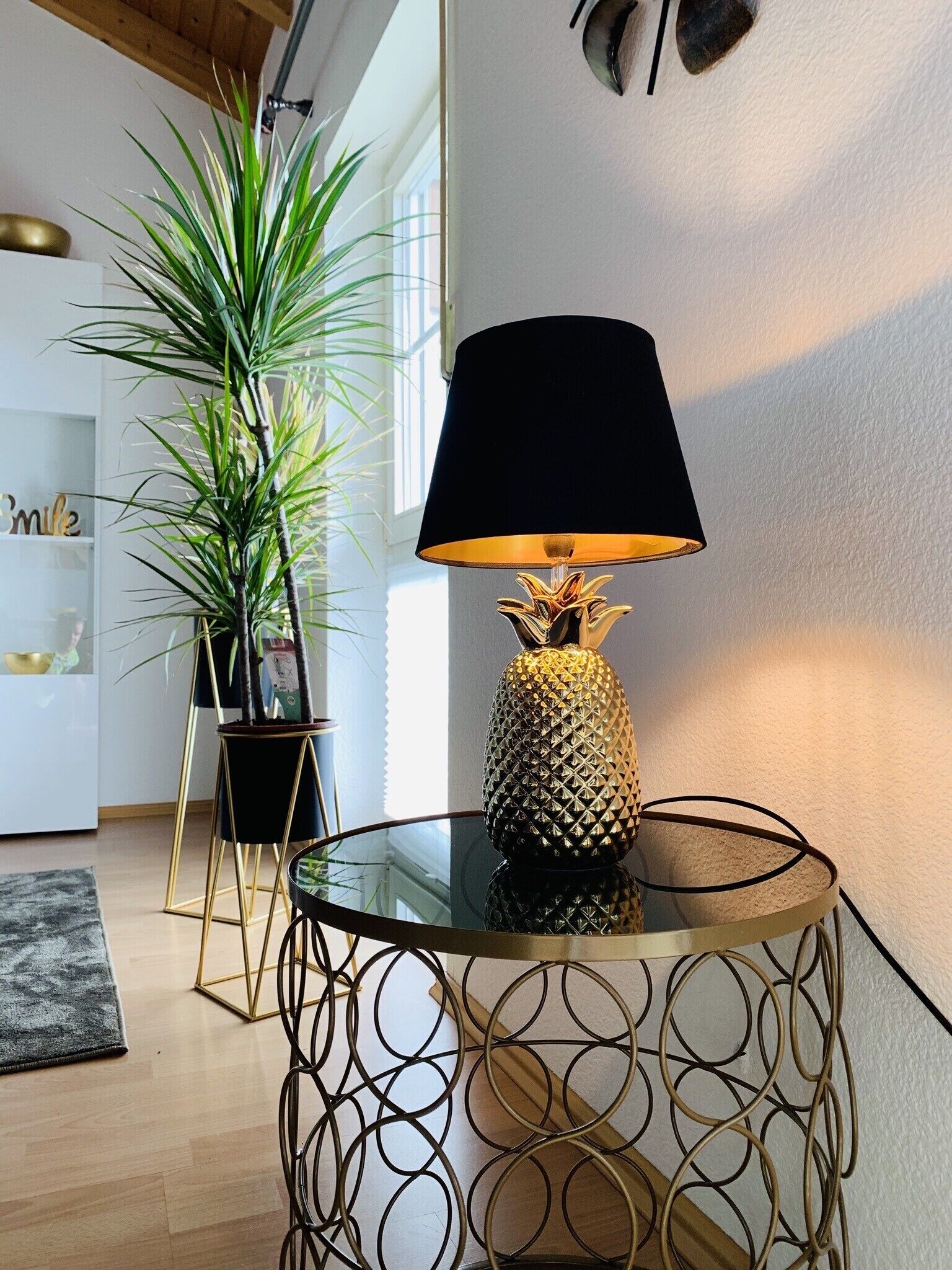 Un salon moderne avec une table en verre, une lampe décorative en forme d’ananas et une grande plante.