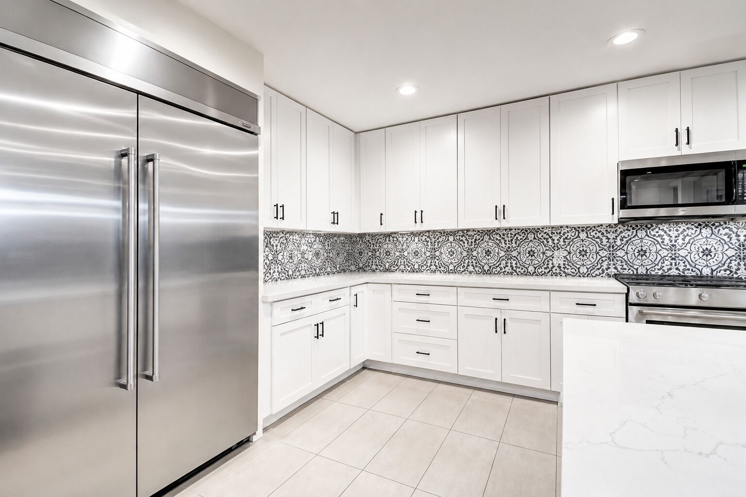 Una cocina moderna con electrodomésticos de acero inoxidable, armarios blancos, salpicadero estampado y piso de baldosas.