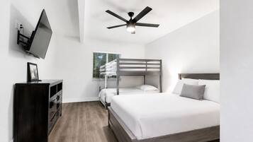 A modern bedroom with a bunk bed, a flat-screen TV mounted on the wall, a ceiling fan, and a wooden dresser.