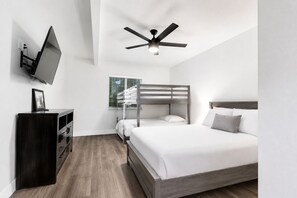Un dormitorio moderno con una cama litera, un televisor de pantalla plana montado en la pared, un ventilador de techo y un aparador de madera.