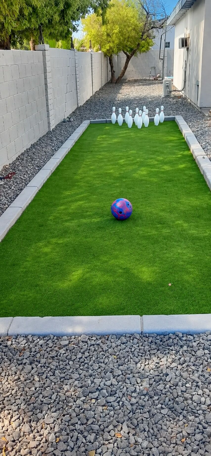 Bolera con césped artificial verde, una bola de boliche y bolos.