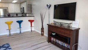 Un soggiorno moderno con pavimento in legno, una TV a parete, una libreria e sgabelli colorati.