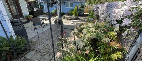 A patio with outdoor furniture, a garden with various plants and flowers, and a house in the background.