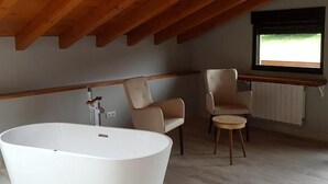 Un baño moderno con una bañera independiente, dos sillas y un ventanal con vistas.