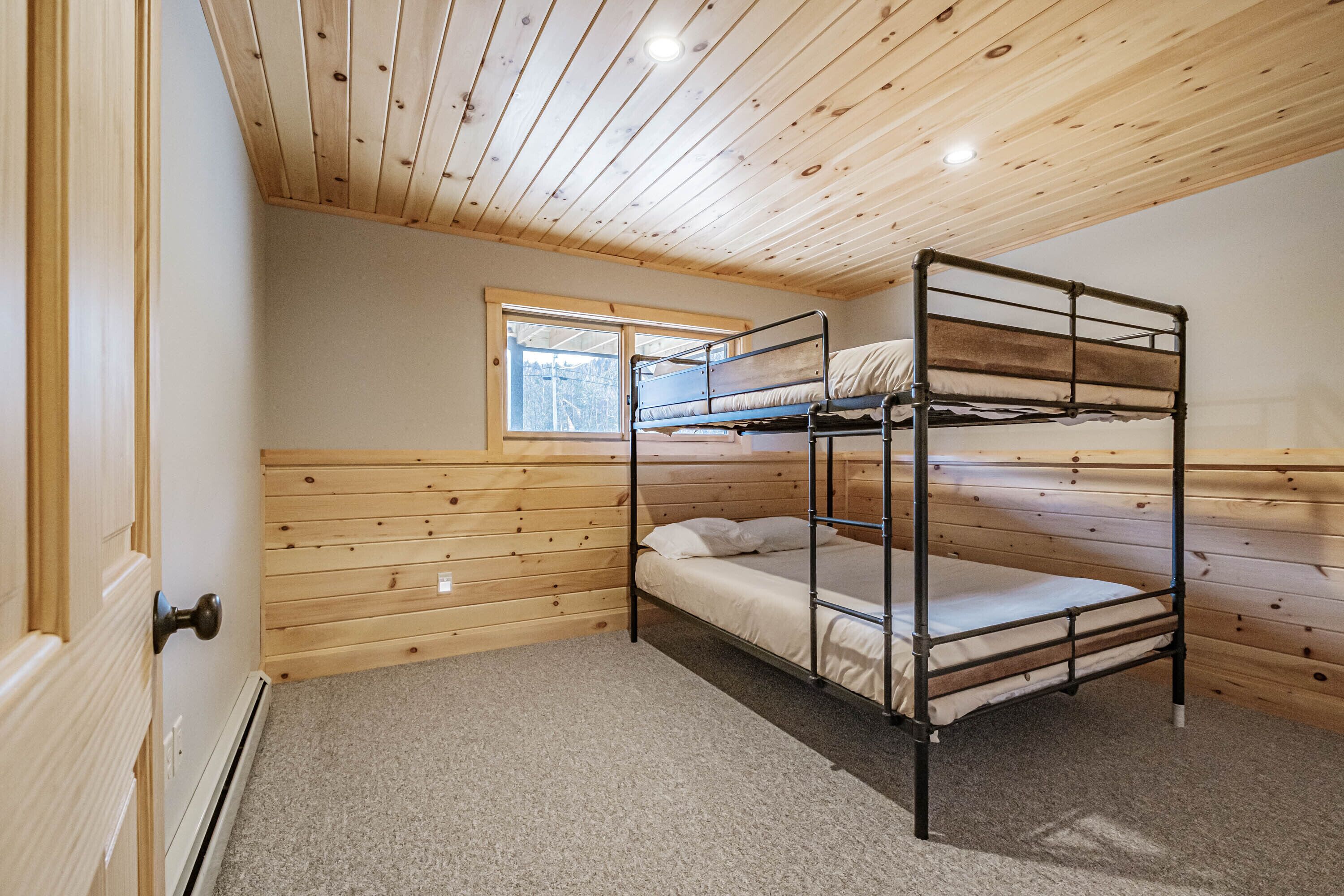 A bunk bed room with wooden walls and a window.