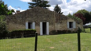 A stone building with a sloped roof, surrounded by a grassy area and a wire fence. - Quiet gite - 20 mn from Royan, 10mn from Saintes (Retaud)