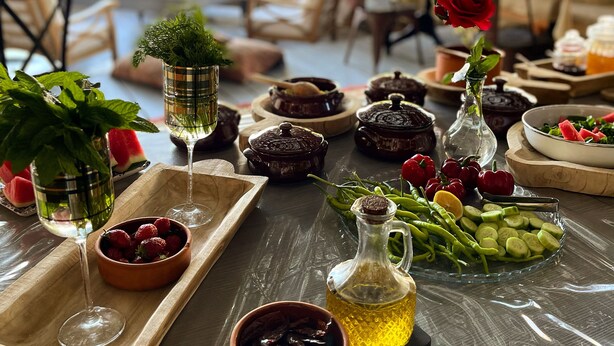 A covered outdoor dining area with tables set for a meal, featuring various dishes, drinks, and fresh produce. - Afet Inn Hotel (Cesme)