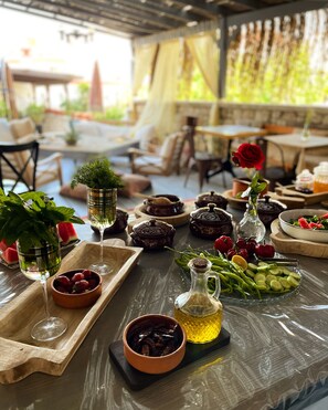 A covered outdoor dining area with tables set for a meal, featuring various dishes, drinks, and fresh produce. - Afet Inn Hotel (Cesme)
