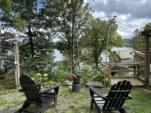 Dos sillas Adirondack mirando un lago, con una terraza de madera y un pabellón al fondo.
