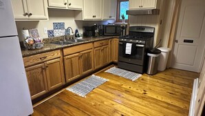 Una cocina con armarios de madera, un refrigerador, un microondas, una estufa y un bote de basura.