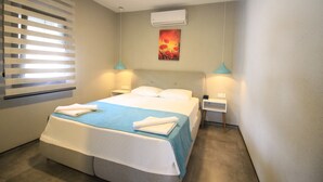 A hotel room with a bed, two bedside tables, an air conditioner, a painting, and a window with blinds. - YALIN APART HOTEL (Bodrum)