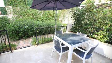 Un patio al aire libre con una mesa, sillas, un paraguas negro y una barandilla de metal.