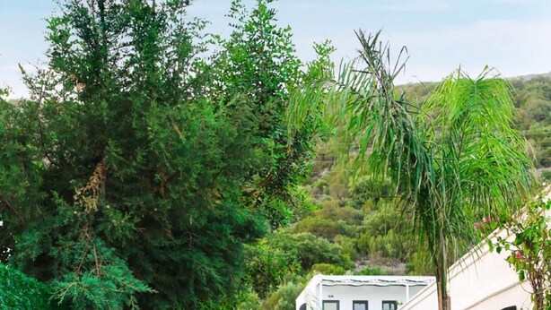 A pathway lined with trees and shrubs leading to a white building with a black awning. - YALIN APART HOTEL (Bodrum)