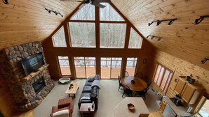 Ein geräumiges Blockhaus-Interieur mit Kamin aus Naturstein, einem großzügigen Wohnbereich mit Sofa und Couchtisch, einem Esstisch mit Stühlen und einer Küchenzeile.