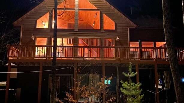 Eine zweistöckige Holzhütte mit einem Balkon im oberen Geschoss, beleuchtet durch warmes Licht.