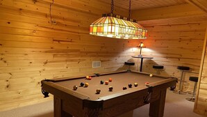 Ein Billardtisch mit Kugeln, eine hängende Stuckleuchte und Holzwände.