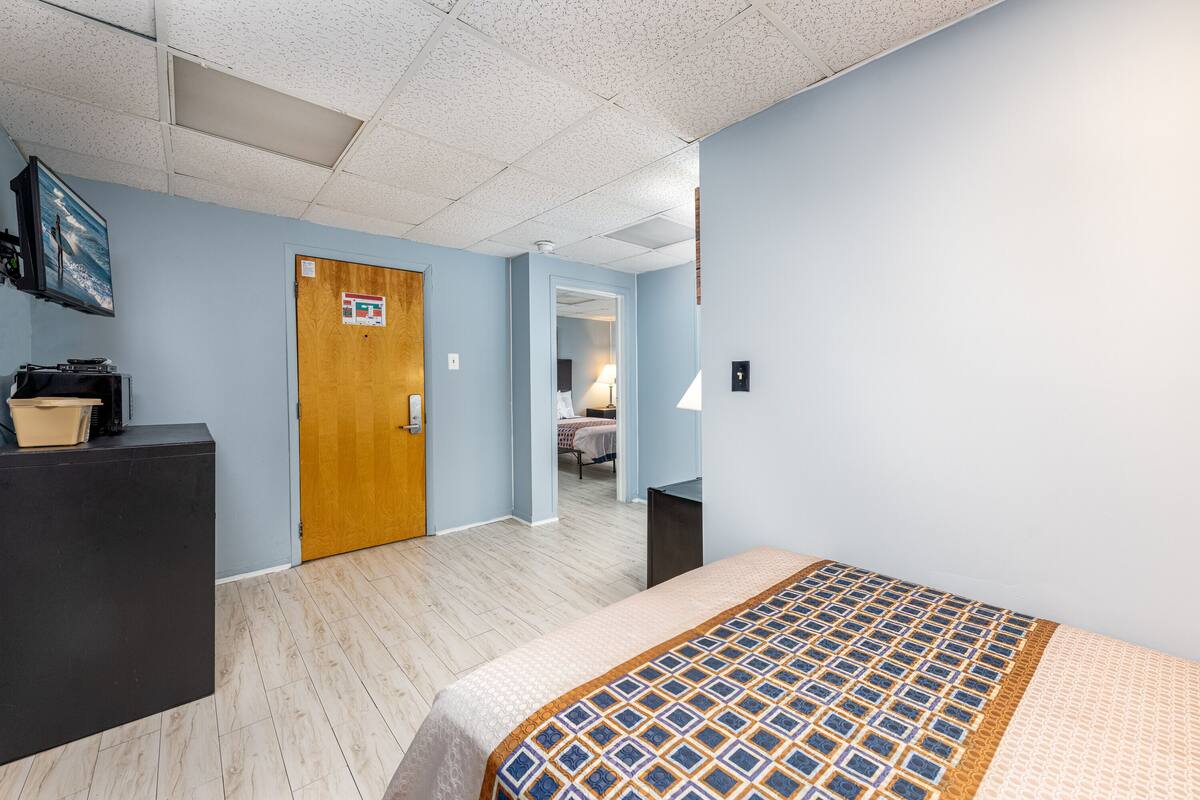 Ein Hotelzimmer mit einem Bett, einem Schreibtisch, einem Schrank und einer Tür zu einem anderen Raum.