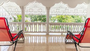 A room with two red chairs facing a white balcony with decorative metal railings and a view of greenery. - Runaway Bay Gem, Spacious and Bright, 5 mins drive to the Beach! (Runaway Bay)