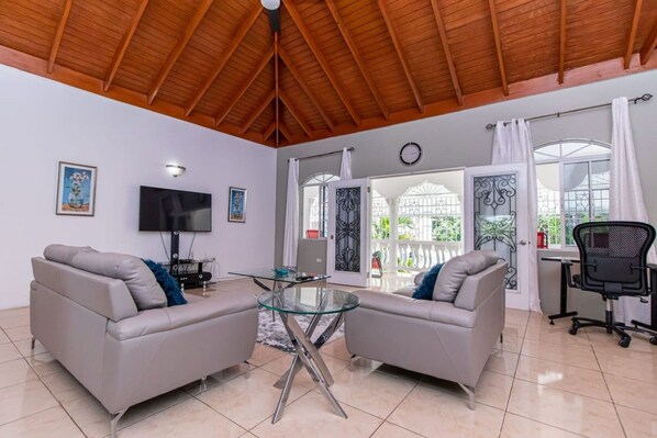 A modern living room with two sofas, a glass coffee table, a flat-screen TV, and a dining area with a glass table.