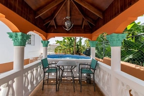 A covered outdoor area with a pool, seating, and a view of the surrounding greenery.