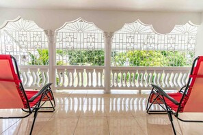 A room with a balcony, two red chairs, and a view of greenery.