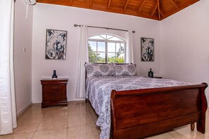 A bedroom with a wooden bed, a nightstand, a window with curtains, and two wall-mounted paintings.