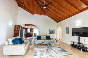 A spacious living area with a high ceiling, a television, and a kitchen in the background. - Runaway Bay Gem! (Runaway Bay)