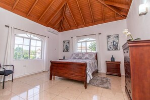 A bedroom with a wooden bed, a dresser, and two windows with curtains.