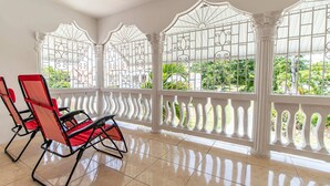 A room with a tiled floor, a red and black chair, and a white balcony with decorative railings. - Runaway Bay Gem, Spacious and Bright, 5 mins drive to the Beach! (Runaway Bay)
