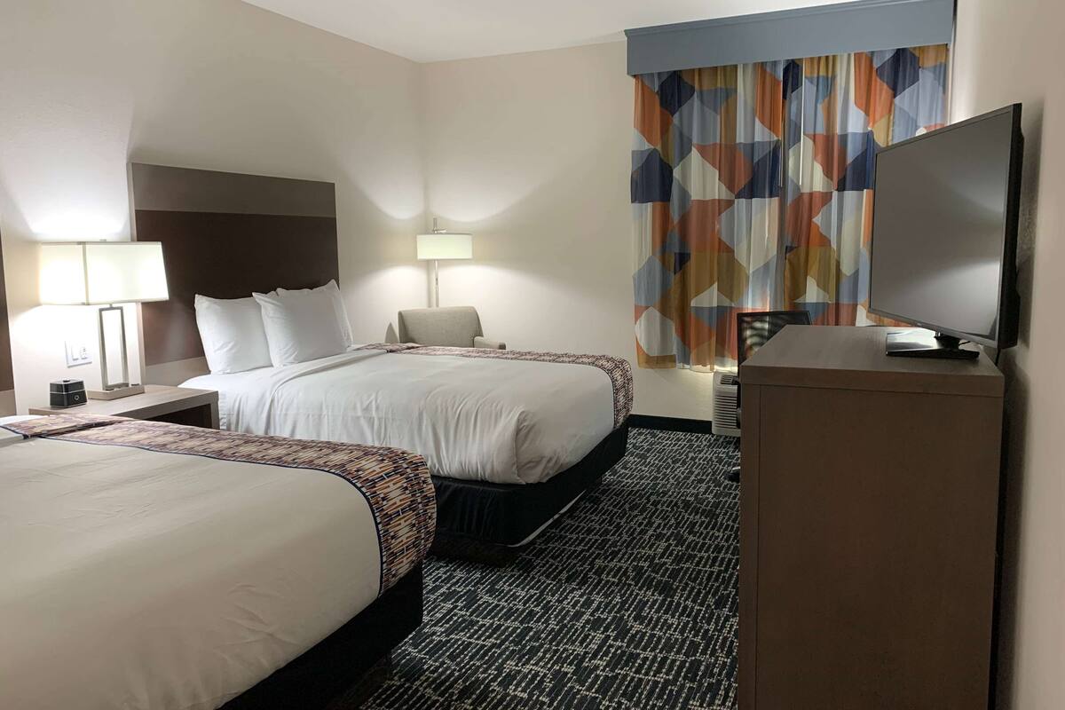 A hotel room with two beds, a flat-screen TV, a desk, and a patterned rug.