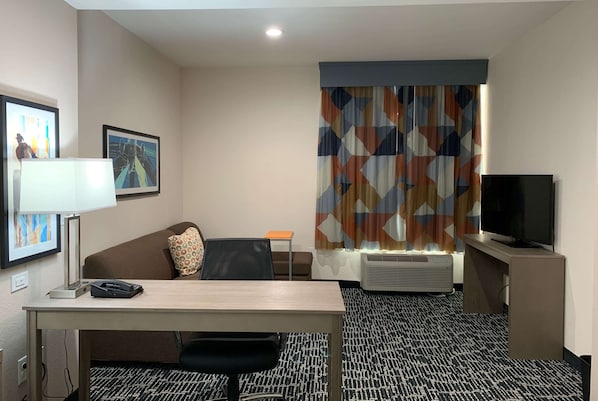 Habitación de hotel con escritorio, silla, televisión, aire acondicionado y alfombra estampada.